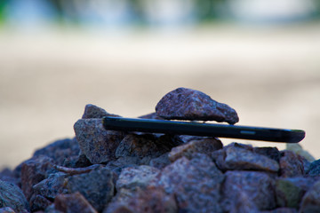 Cell phone with broken glass on gravel granite stones, unbreakable gadget