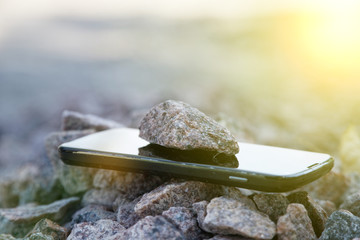 Cell phone with broken glass on gravel granite stones, unbreakable gadget, sun beam lights