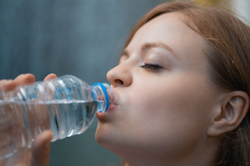 Closeup portrait of young caucasian woman drinking water from a plastic bottle