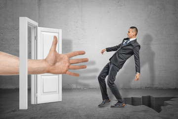Big male open hand reaching through white doorway to catch young businessman who is falling into...