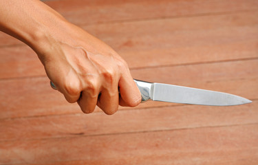 Hand holding knife against plank wood