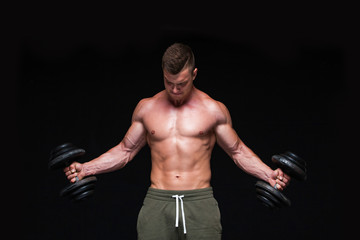 Fototapeta na wymiar Handsome power athletic man with dumbbell confidently looking forward. Strong bodybuilder with six pack, perfect abs, shoulders, biceps, triceps and chest. Strong Athletic Man - Fitness Model showing
