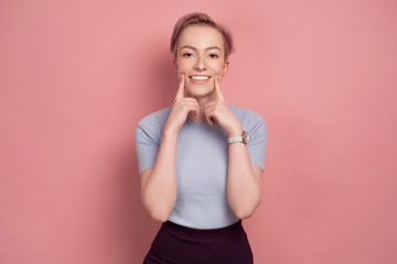 Pink-haired young woman looks at the camera pulling a smile on her face, pink background