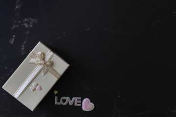 Flat lay of black marble background decorates with shining pink white pearl of hearts and letter of LOVE and small beige pearl gift box