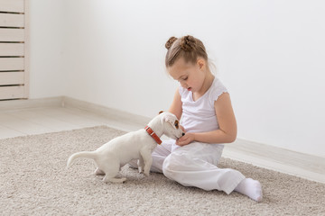 Children, pets and animals concept - little child girl in pajamas playing with Jack Russell Terrier puppy on the floor