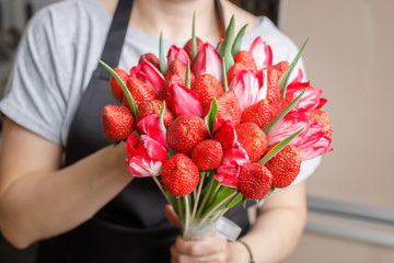 Woman holds in her hands an almost made unique bouquet of tulips and strawberries