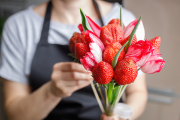 Woman makes an original bouquet of beautiful tulips and ripe strawberries