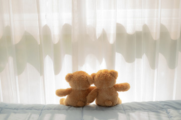 couple bear doll sitting and hug on the bed near the window and curtain