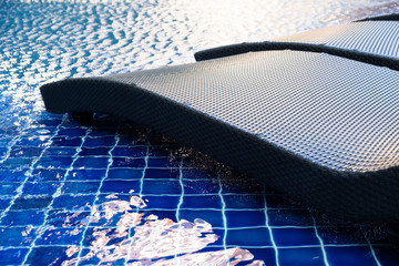 close up rattan pool chair beside the swimming pool with the blue water and sun light reflection