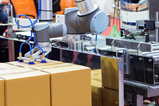 The robot arm transfers carton box  to conveyor line