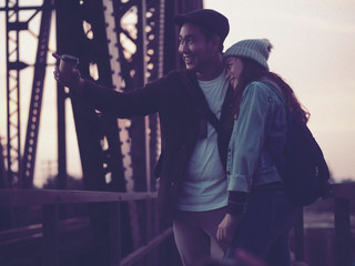 Happy Asian tourist couple drinking takeaway coffee cup with black iron bridge background.