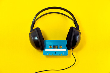 Top view of Headphone and blue classic tape cassette against yellow isolated background. Listening music theme.