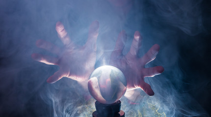 The hands of a fortune teller and a glass ball can be seen against a black background. Smoke or fog...