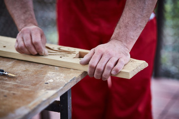 Closeup of male hands carpenter using sandpaper to sand wooden detail.