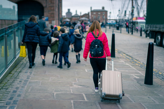 Blurred photo,The asian girl with pink jacket walks along street carries luggage with children in background in Albert, Liverpool, England, United Kingdom