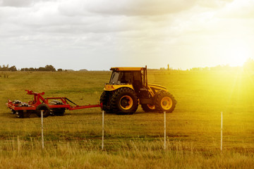 Fototapeta premium Tractor drags a grinder during sunset on a farm
