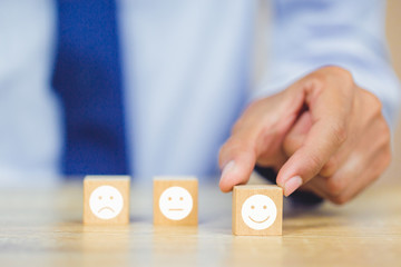 customer pressing smiley face emoticon on wood cube, Service rating, satisfaction concept.