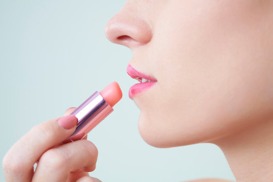 Close-up image of woman applying light peach lip balm to keep lips moisturized