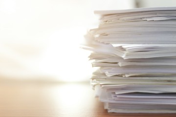 Paper stack on desk related to business functions. Paper-related work on the table.