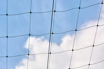 Black volleyball net against the blue sky with clouds.