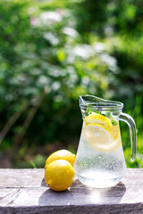 fresh lemonade and two lemons on wooden old table against a green grass background