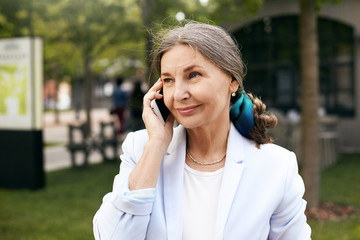 Elegant attractive mature businesswoman wearing white jacket and headscarf in her gathered hair...