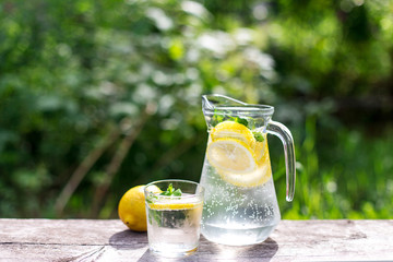 fresh lemonade, glass and one lemon on wooden old table against a green grass background