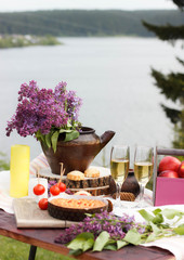 Healthy picnic for a summer vacation with freshly baked croissants, fresh fruit and fruit salad, homemade cake, flowers and white wine. Picnic on the rever.