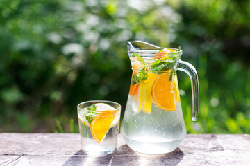 fresh lemonade with orange and a glass on wooden old table against a backdrop of green grass