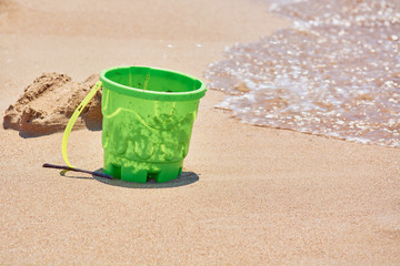 Toy for children green bucket on sandy shore of beach with sea waves.