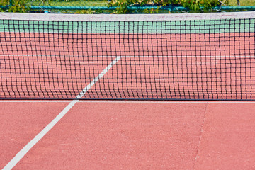 Black stretched net on red tennis court for game.