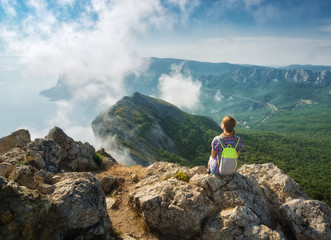 Girl hiker with backpack sitting on a cliff edge