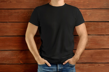 Brawny slim guy in a black T-shirt and blue jeans on a brown wooden studio background.