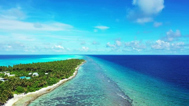 Aerial view of a tropical island with a forest and village on it. In the turquoise sea in Bali. Next to a reef. Dolly out