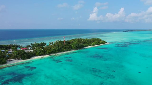 Aerial view of a tropical island with a forest, village and radio mast on it. In the turquoise sea in Bali. Pan left