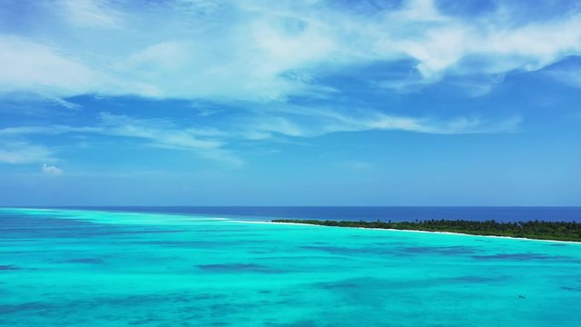 Aerial view of the turquoise sea in the Maldives. With an island in it  under a cloudy sky. Truck left.