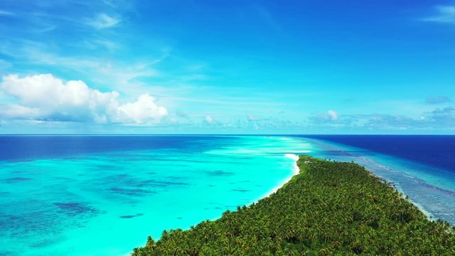 Aerial view of a tropical island with a forest on it. In the turquoise sea in Bali. Next to a reef. Some clouds in a blue sky. flight sideways, truck left.