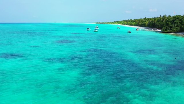 Aerial view of the turquoise blue sea in Bali. An island to the left with some boats anchoring next to it. Dolly in.