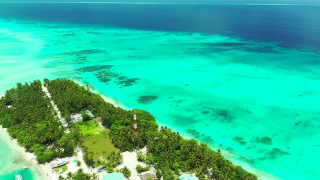 Aerial view flying over a thin tropical island with a village on it. Surrounded by the turquoise sea of the Gulf of Thailand. Looking down, diagonal flight.