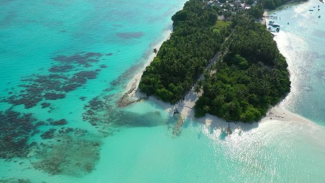 Aerial view of a tropical island with a forest of palm tree divided by a sandy path. In the turquoise sea in Hawaii. Looking down on it. A village in the distance on the island.