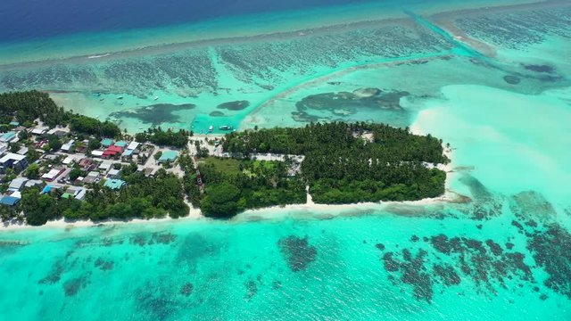 Aerial view flying over a thin tropical island with a village on it with a forest of palms. Surrounded by the turquoise sea of the Gulf of Thailand. Looking down, truck right