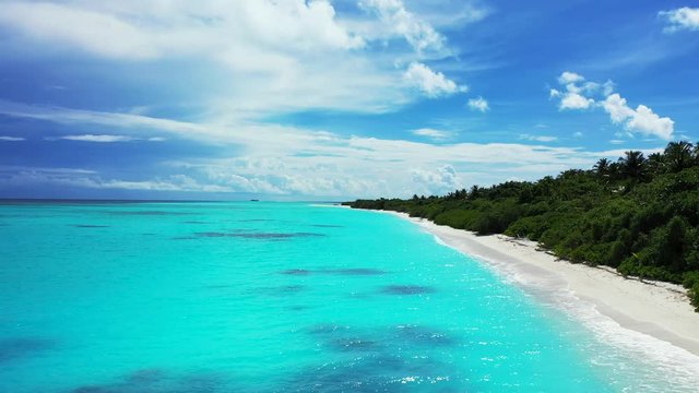 Aerial view of a flight along a tropical island with palm trees on it. A beach next to turquoise water, soft waves. The Bahamas under. Dolly in