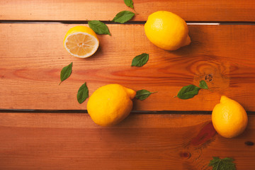 Group of yellow lemons and leaves are laying on a wooden surface