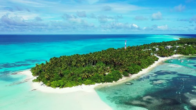 Aerial view of a tropical island with a forest of palm trees. In the turquoise sea in Hawaii. A village on it. Reefs in the water pan left