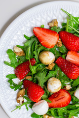 Salad with mozzarella cheese, arugula and strawberries on a white plate. Healthy summer green salad for diet, snack or light dinner.
