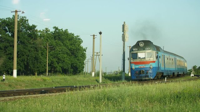 Light blue train moving across a grassy area on a sunny day in summer  