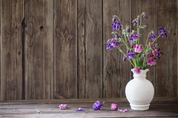 aquilegia flowers in white vase on old wooden background