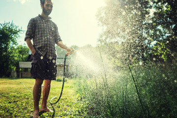 Hipster young man watering plants in a country house, summer and garden care