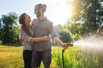 Young beautiful couple watering the plants in a country house, summer, work in the garden, love and...