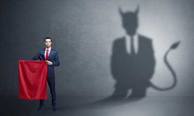 Businessman standing with red cloth in his hand and devil shadow on the background
